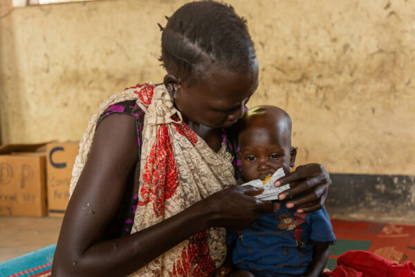 Mother is Feeding her child with plumbee nuts at a health facility in Bentiu.