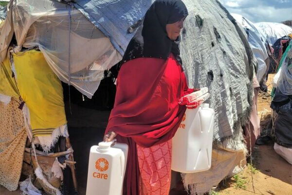 Dadaab Refugee Camp - outskirts - this is where the new arrivals, that have not been registered yet, settle. Fatuma, 60, is a new arrival at Dadaab. She arrived two months ago from Mogadishu in Somalia together with 12 members of her family. She is carrying two CARE jerricans and a package of soap bars, that have been distributed by CARE.

&ldquo;There are no usable latrines for us, so we have to just go where we can. And we drink from the same water human and animal feces have been washed into. Some of my neighbors have gotten sick and are in the hospital,&rdquo; describes Fatuma. In April this year, there have already been more than 1,000 confirmed cases of Cholera. Fatuma is not registered yet and lives in the outskirts with about 133.000 other new arrivals. &ldquo;We came from Mogadishu, where my husband died in an explosion. There we had no security and no education. It was very hard. It took us eight days to come here. We saved the money for a truck to the border, then we walked the rest.&rdquo;&nbsp;
Eight family members fit in the small about 4m&sup2; makeshift hut made from sticks and cloth from old clothes that she and her children built themselves. &ldquo;We have no supplies, everything here we either found or neighbors gave to us. It is not big enough for my whole family. Five of the boys sleep outside,&rdquo; says Fatuma. The cloth and tarps that make up her home are not waterproof. The heavy rains completely flood her hut. Every night she sits inside with her three grandchildren under her clothes, and they pray, that the roof does not collapse on top of their heads. &ldquo;It was painful to leave home, even talking about it now, my emotions come up. But where else should we go? At home in Somalia is nothing left, only fear and trauma.&rdquo;
Living in the outskirts of the official camp is a challenge for Fatuma. Access to water, food, and basic items such as soap is limited. There are not enough resources for the many people in need. The distribution of soap and jerricans has been cancelled for three months in a row, because the resources are missing. CARE has stepped in and started distributing to new arrivals. &ldquo;Without CARE we would have nothing. Now we at least have access to some drinking water, soap, and jerricans&rdquo;, says Fatuma. However, the drinking water in the tanks built by CARE is not enough for everyone. Water deliveries are also delayed due to the current floods in Dadaab. &ldquo;When there is no water in the tanks, we sometimes walk for 1.5 hours to go and find water. Then we roll the water back to our hut,&rdquo; describes Fatuma. Rolling the water means that the round jerricans are put on the floor and rolled either by hand or by foot through mud, dirt, and feces. The clean drinking water easily contaminates this way and can cause serious illnesses. That is why CARE distributes rectangular jerricans, with an easy handle to carry, so the water stays clean and safe.

CARE supports the new arrivals with the supply and installation of micro water storage facilities which can hold to up to 5,000 liters of drinking water and distributes plastic jerricans, constructs communal latrines and supplies soap bars to all new arrival households residing in the outskirts. Additionally, women and girls are provided with menstrual hygiene dignity kits.